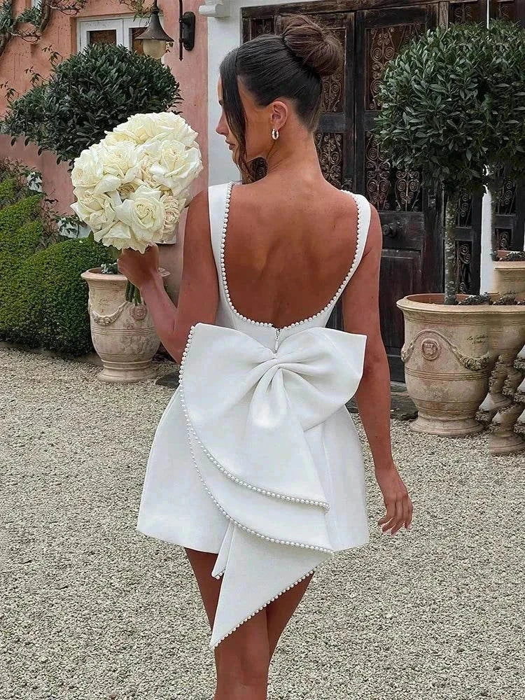 Vestido Mini branco em crepe com corte evasê, decote profundo nas costas, bordado de pérolas e laço grande assimétrico