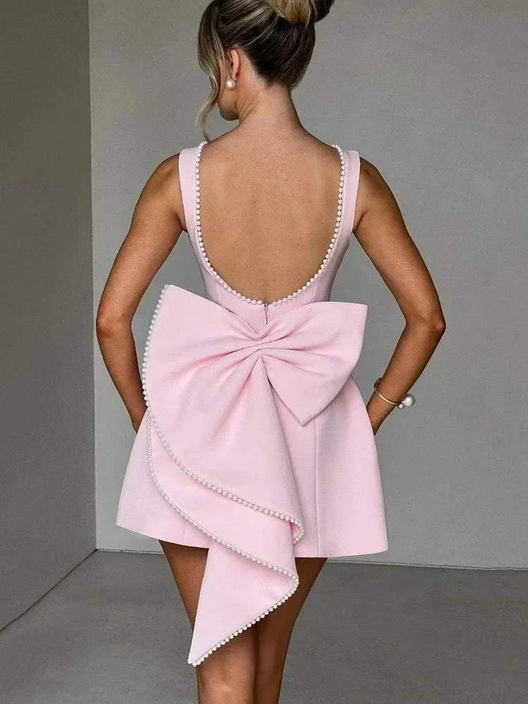 Vestido Mini rosa poudré em crepe com decote profundo nas costas, adornado com pérolas e laço assimétrico