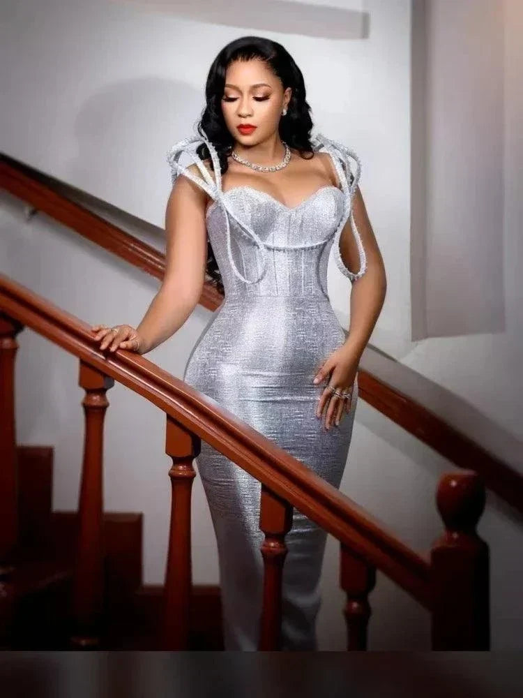 Vestido prateado comprido de tecido metalizado, com corpete estruturado e detalhes esculturais rígidos nos ombros