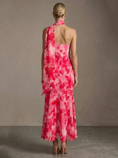 Vestido longo floral rosa com decote assimétrico e echarpe fluida no pescoço.