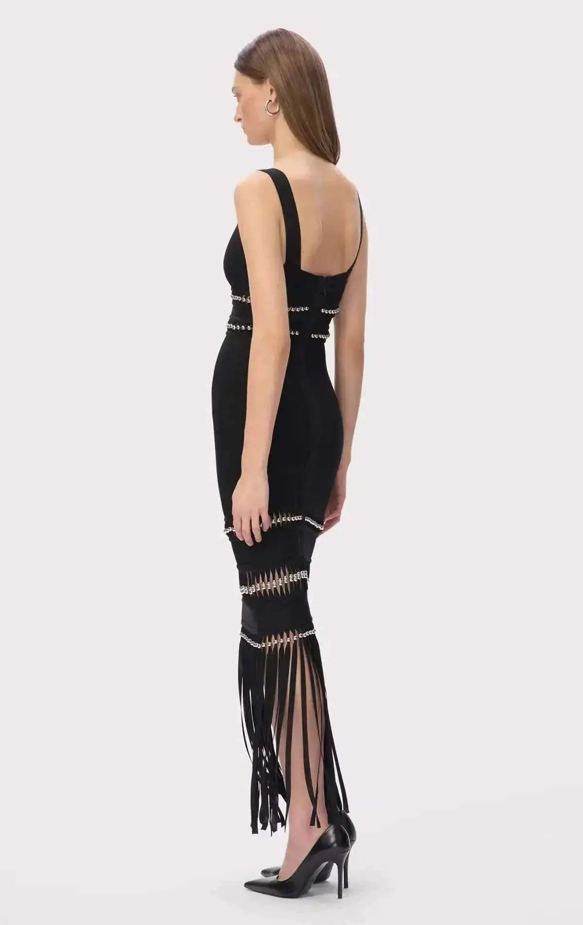 Vestido Bandagem preto e justo, sem mangas, com tiras decorativas prateadas e longas franjas na bainha.