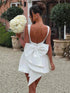 Vestido Mini branco em crepe com corte evasê, decote profundo nas costas, bordado de pérolas e laço grande assimétrico