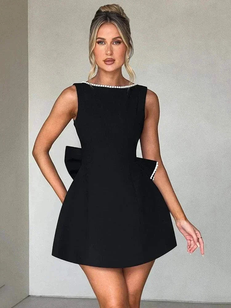 Vestido Mini preto em tecido crepe com corte evasê, decote canoa adornado com pérolas e laço estruturado lateral