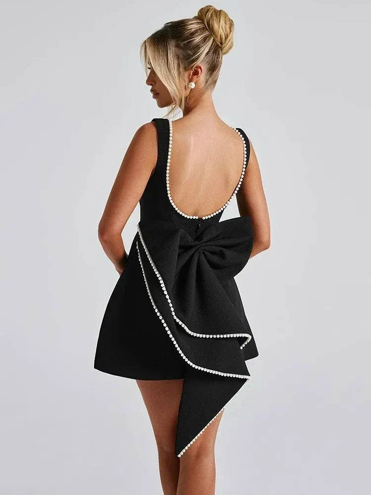 Vestido Mini preto em tecido crepe com decote profundo nas costas, acabamento com pérolas e grande laço assimétrico