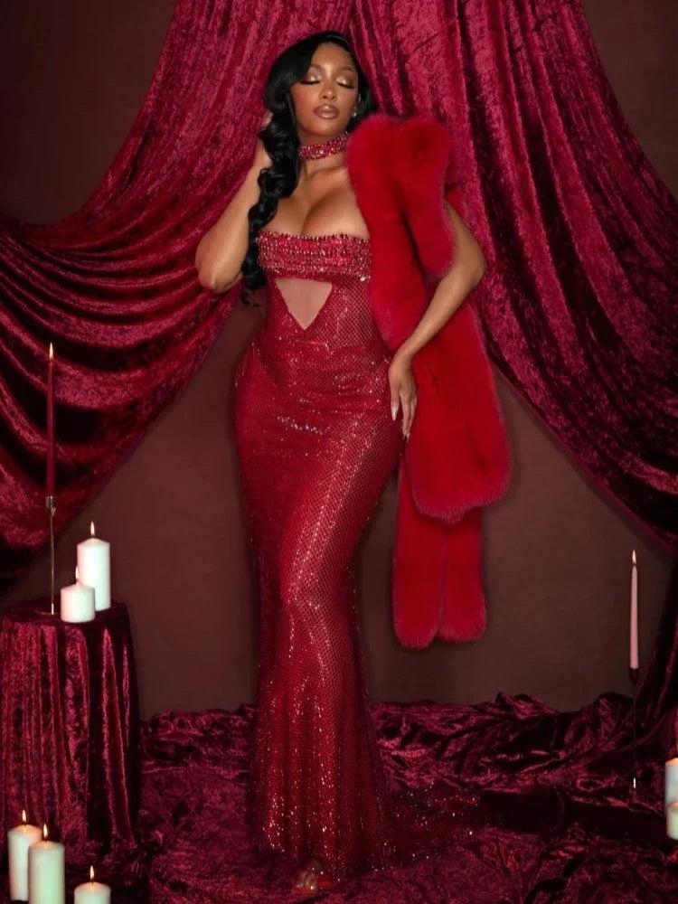 Vestido Rubi comprido em vermelho, justo e coberto de pedrarias brilhantes, com decote cai-cai e recorte triangular